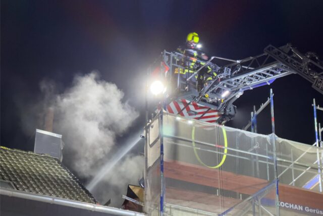 Ein Feuerwehrmann löscht über eine Drehleiter einen Dachstuhlbrand in Marl-Hüls.