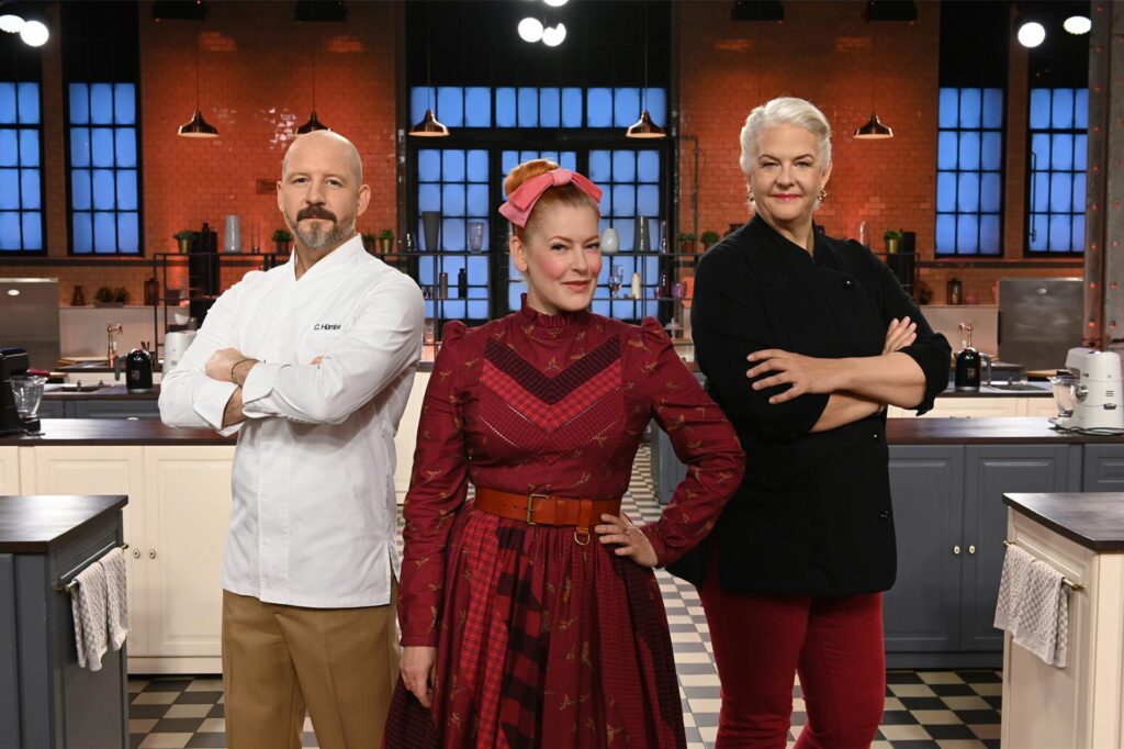 Christian Hümbs (Jury), Enie van de Meiklokjes (Moderatorin) und Bettina Schliephake-Burchardt (Jury) stehen in der Kulisse von 