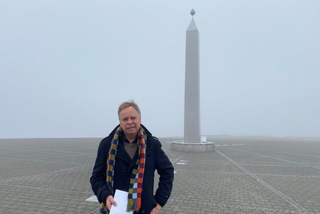 Volker Lindner im dunklen Mantel mit buntem Schal am Sonnenuhr-Obelisken auf der Halde Hoheward in Herten.