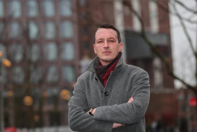Der AfD-Politiker Matthias Helferich steht vor dem Dortmunder U-Turm und schaut mit verschränkten Armen in die Kamera.