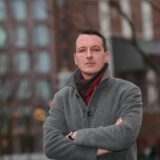 Der AfD-Politiker Matthias Helferich steht vor dem Dortmunder U-Turm und schaut mit verschränkten Armen in die Kamera.
