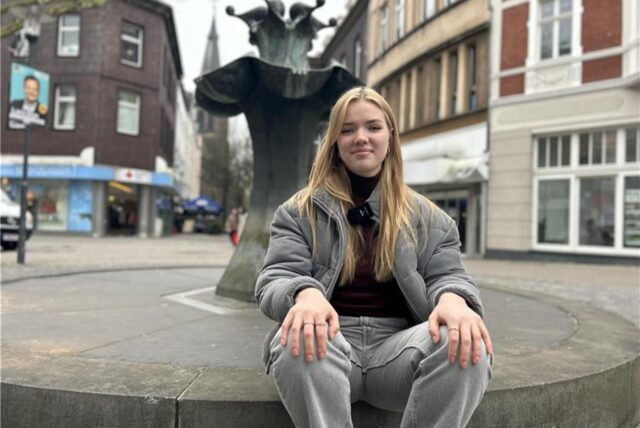 Eine junge Frau, die an einem Brunnen sitzt.