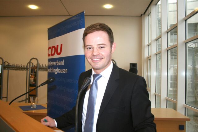 Ein Mann im Anzug steht hinter einem Pult und lächelt in die Kamera. (Archivbild)