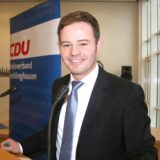 Ein Mann im Anzug steht hinter einem Pult und lächelt in die Kamera. (Archivbild)