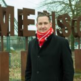 Brian Nickholz, SPD-Bundestagsabgeordneter, steht vor einem Schriftzug aus Bronze, der das Wort „Mensch“ bildet, neben der La Victoria Eventhalle auf dem ehemaligen Schachtgelände AV 1/2 in Marl.