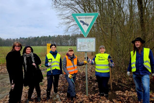Sechs Menschen mit Warnwesten vom Naturschutzbund stehen mit Schaufeln an einem Waldrand.