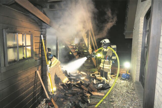 Feuerwehrleute löschen mit einem C-Rohr den Brand an einer Gartenhütte.