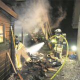 Feuerwehrleute löschen mit einem C-Rohr den Brand an einer Gartenhütte.