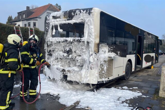 Ein Bus steht nach einem Brand auf dem Schneer Weg in Witten. Das Heck ist mit Löschschaum bedeckt. Zwei Feuerwehrleute sind zu sehen, die Schaum aufbringen.