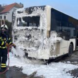 Ein Bus steht nach einem Brand auf dem Schneer Weg in Witten. Das Heck ist mit Löschschaum bedeckt. Zwei Feuerwehrleute sind zu sehen, die Schaum aufbringen.