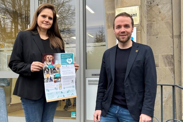 Bürgermeister Marcel Mittelbach und Christina Rode mit einem Plakat der Assistenzhunde-Kampagne vor dem Haupteingang zum Rathaus-Altbau.