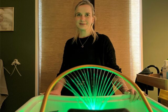 Denice Köse steht vor dem Head-Spa-Gerät, es läuft Wasser heraus und leuchtet grün.