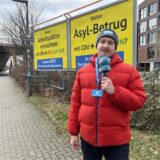 Reporter Tim Hübbertz steht vor zwei gelben Wahlplakaten mit Slogans für die AfD.