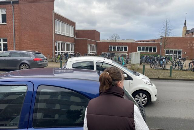 Nicole Heße schaut zwischen parkenden Autos an der Gartenstraße in Herten-Mitte auf das gegenüber liegende Gymnasium.