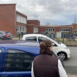 Nicole Heße schaut zwischen parkenden Autos an der Gartenstraße in Herten-Mitte auf das gegenüber liegende Gymnasium.