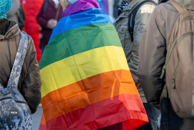 Eine Demonstrantin hat eine Regenbogenflagge über die Schultern gelegt.