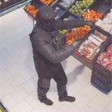 Ein schwarz gekleideter und vermummter Mann steht vor dem Obstregal eines Supermarktes.