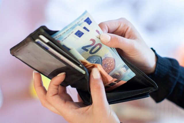 Nahaufnahme von zwei Händen, die Geldscheine aus einem Portemonnaie hervorholen.