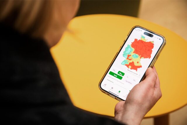 Eine Frau hält ein Handy in der Hand, das eine rote Feinstaub-Karte von Deutschland zeigt.