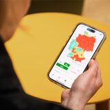 Eine Frau hält ein Handy in der Hand, das eine rote Feinstaub-Karte von Deutschland zeigt.
