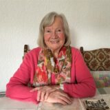 Renate Bystron sitzt an ihrem Esstisch, vor sich Fotos und Dokumente.