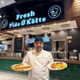 Erhan Kafali hält vor dem Gastronomie-Stand „Fresh Pide & Köfte“ im Palais Vest in Recklinghausen zwei mit Gerichten gefüllte Teller in den Händen.