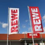 Flaggen mit dem Rewe-Schriftzug vor einer Filiale des Supermarkts.