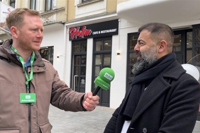 Mehmet Akpinar steht vor seinem neuen Restaurant, ein Reporter hält ihm ein Mikrofon hin.