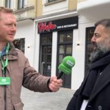 Mehmet Akpinar steht vor seinem neuen Restaurant, ein Reporter hält ihm ein Mikrofon hin.