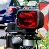 Ein mobiles geschwindigkeitsmessgerät steht am Straßenrand. Im Hintergrund ist der Seitenstreifen, sowie ein Auto dass von der Kamera wegfährt zu sehen. Weitere Autos kommen aus der entgegengesetzten Fahrtrichtung.
