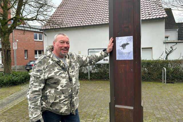 Ein Mann lehnt mit der linken Hand an einem Pfahl in Datteln Ahsen. Am Pfahl prangt ein laminiertes Papier mit dem Text: „Herrchen oder Frauchen räumt es selbstverständlich weg!“