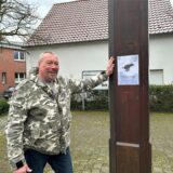 Ein Mann lehnt mit der linken Hand an einem Pfahl in Datteln Ahsen. Am Pfahl prangt ein laminiertes Papier mit dem Text: „Herrchen oder Frauchen räumt es selbstverständlich weg!“