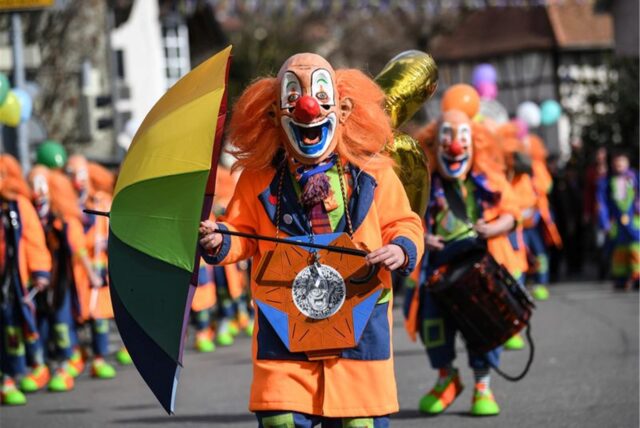 Ein Mensch steht als Clown verkleidet auf einer Straße.