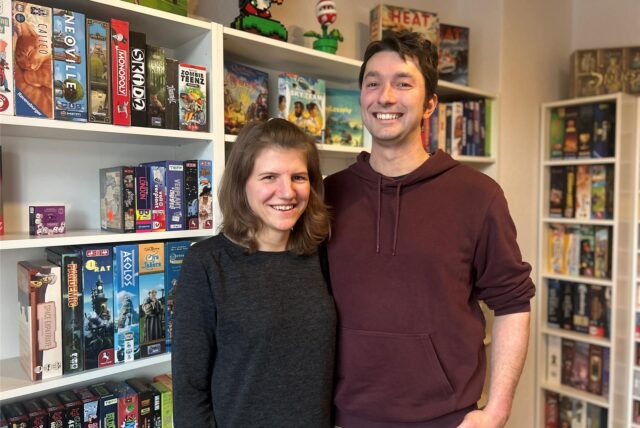 Jennifer und Johannes stehen vor einem großen Regal voll mit verschiedenen Spielen.