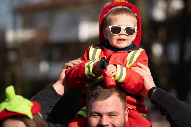 Ein kleiner Junge im Feuerwehrkostüm sitzt bei seinem Vater im Nacken