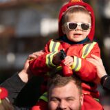 Ein kleiner Junge im Feuerwehrkostüm sitzt bei seinem Vater im Nacken