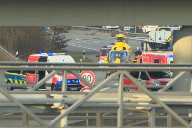 Neben einer Autobahnbrücke steht ein gelandeter Rettungshubschrauber zwischen mehreren Rettungs- und Polizeifahrzeugen.