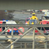 Neben einer Autobahnbrücke steht ein gelandeter Rettungshubschrauber zwischen mehreren Rettungs- und Polizeifahrzeugen.