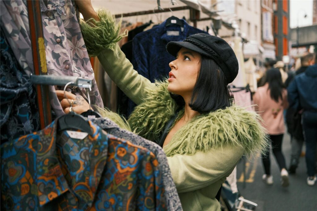 Eine Frau in grüner Felljacke und schwarzer Mütze schaut sich bunte Hemden auf einem Trödelmarkt in NRW an. Eine Frau in grüner Felljacke und schwarzer Mütze schaut sich bunte Hemden auf einem Trödelmarkt in NRW an.