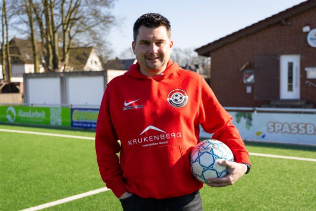 Daniel Pyszny trägt einen roten Pullover und hält einen Ball in seiner linken Hand.