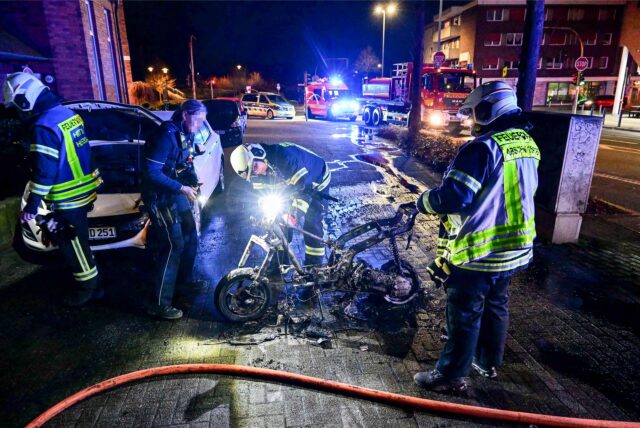 Einsatzkräfte der Feuerwehr und Polizei stehen an dem niedergebrannten Roller an der Schlägel-und-Eisen-Straße in Herten.