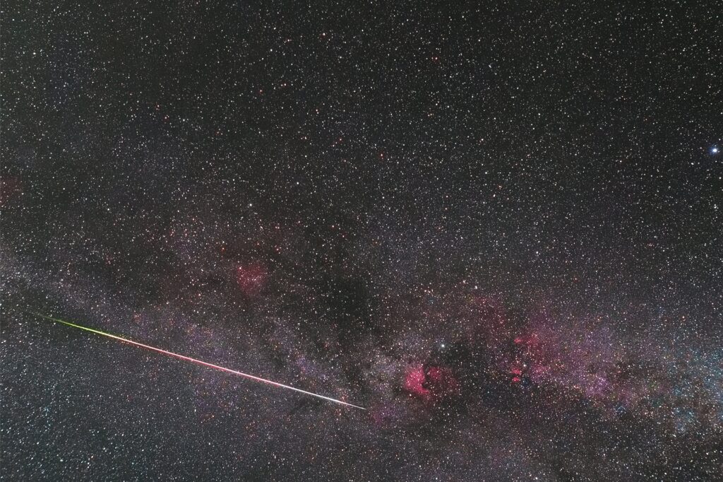 Meteor in der Milchstraße mit roten Wasserstoffnebeln.