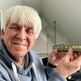 Franz-Josef Hauke hält eine kleine Straßenbahn neben seinen Kopf.