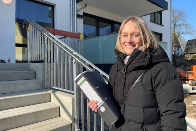Daniele Moge, die sich um die Vermietung der neuen Wohnungen in der Neu-Crengeldanz-Straße in Lütgendortmund kümmert, steht mit einem Aktenordner in der Hand am Treppenaufgang zu einem der neuen Häuser.