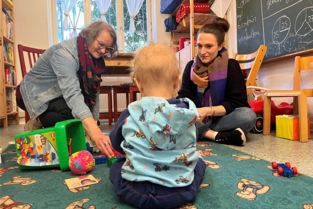 Gina Beck (r.), ihr Sohn Benjamin und Diplom-Sozialarbeiterin Martina Lupatsch sitzen auf einem Teppich und spielen.