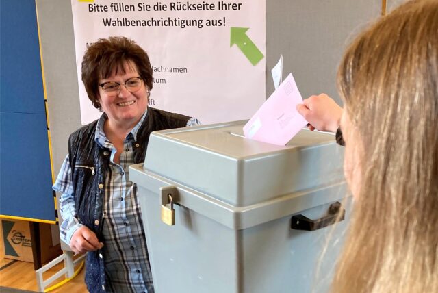 Brigitte Rode steht im Briefwahlbüro im Hertener Rathaus hinter einer Urne, während eine Frau einen Umschlag in diese einwirft.