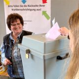 Brigitte Rode steht im Briefwahlbüro im Hertener Rathaus hinter einer Urne, während eine Frau einen Umschlag in diese einwirft.