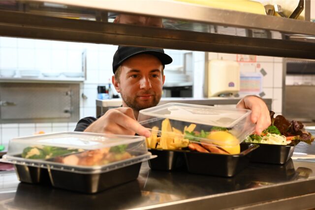 Küchenchef reicht Mehrweggeschirr über die Theke