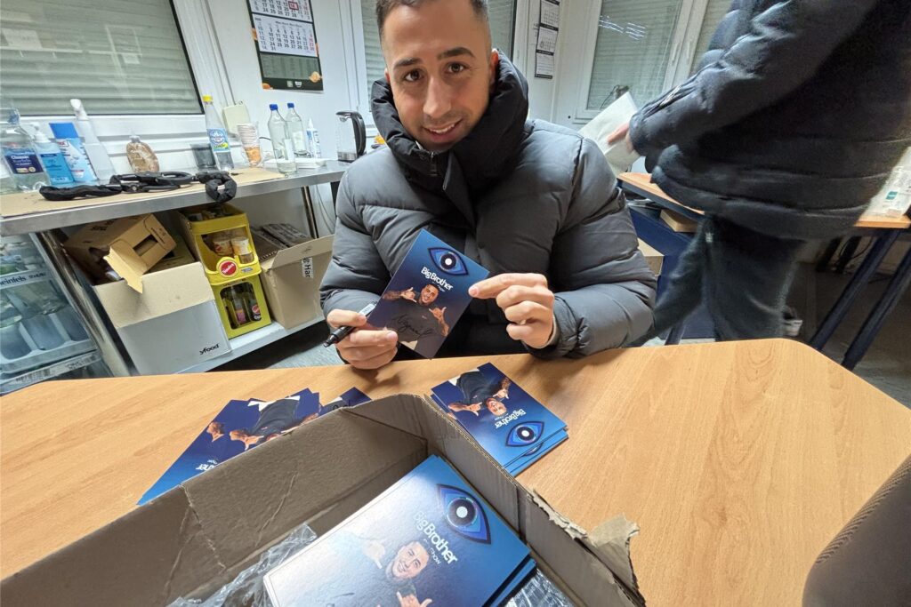 NAdiem Bahjat an einem Tisch mit seinen Autogrammkarten der Big Brother Show.