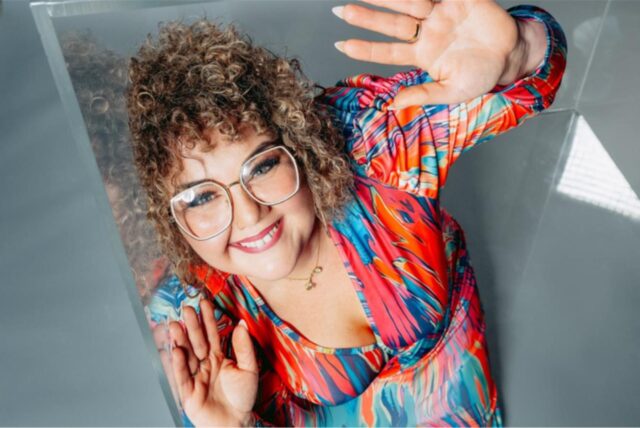 Die Dortmunderin Ulrike (41) lächelt in die Kamera. Sie hat gelocktes Haar, trägt eine Brille und ein buntes Kleid. Sie nimmt an der neuen Staffel des Reality-Formats „Big Brother“ teil.